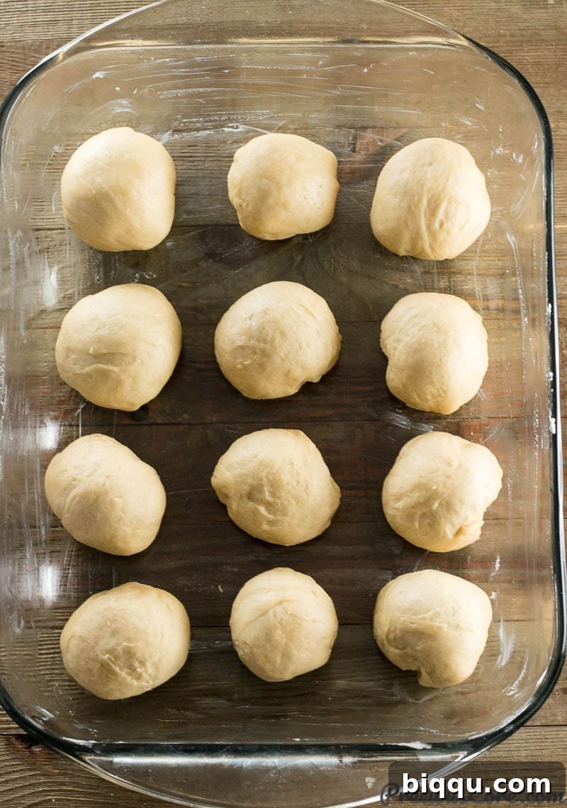 Twelve evenly shaped dough balls arranged in a baking pan, ready for their second rise.