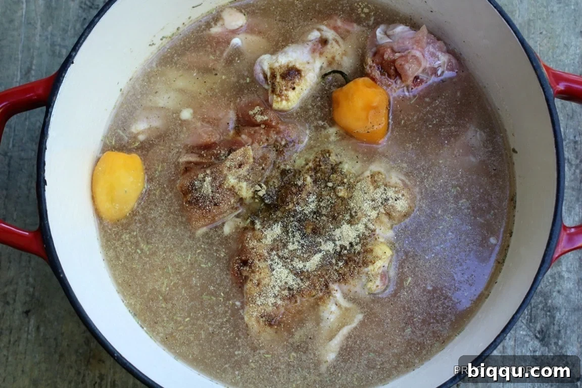 Raw chicken pieces in a pot, covered with water and fresh blended spices before cooking.