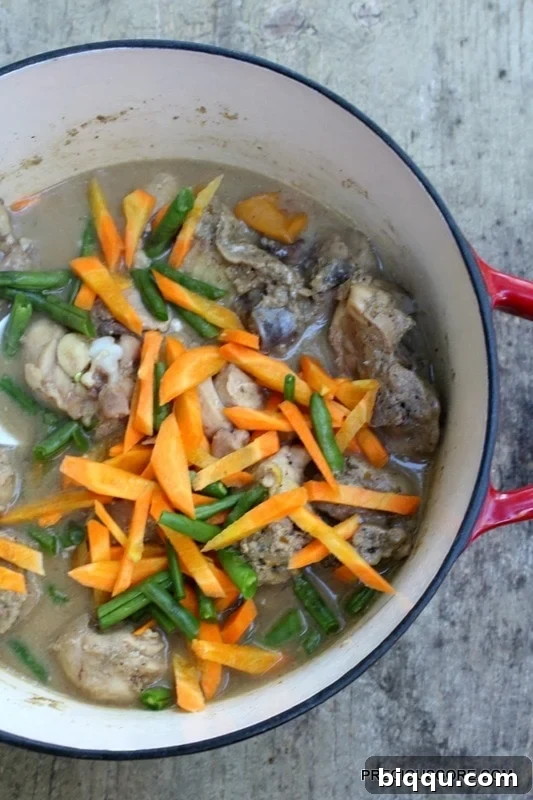 Chicken pepper soup with added fresh carrots and green beans, simmering.