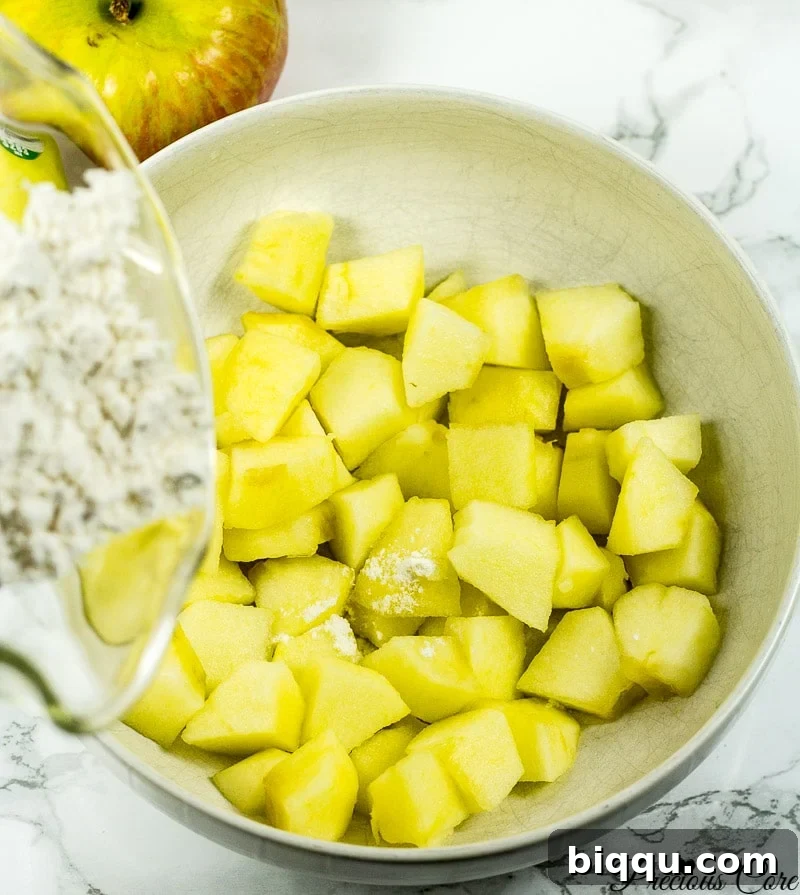Adding flour to chopped apple chunks in a bowl.