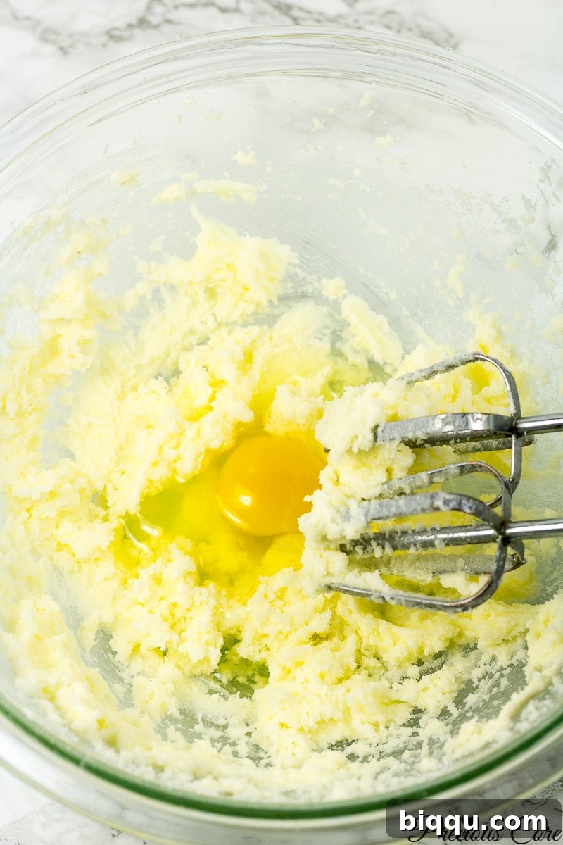 Eggs being added one by one to the creamed butter and sugar mixture.