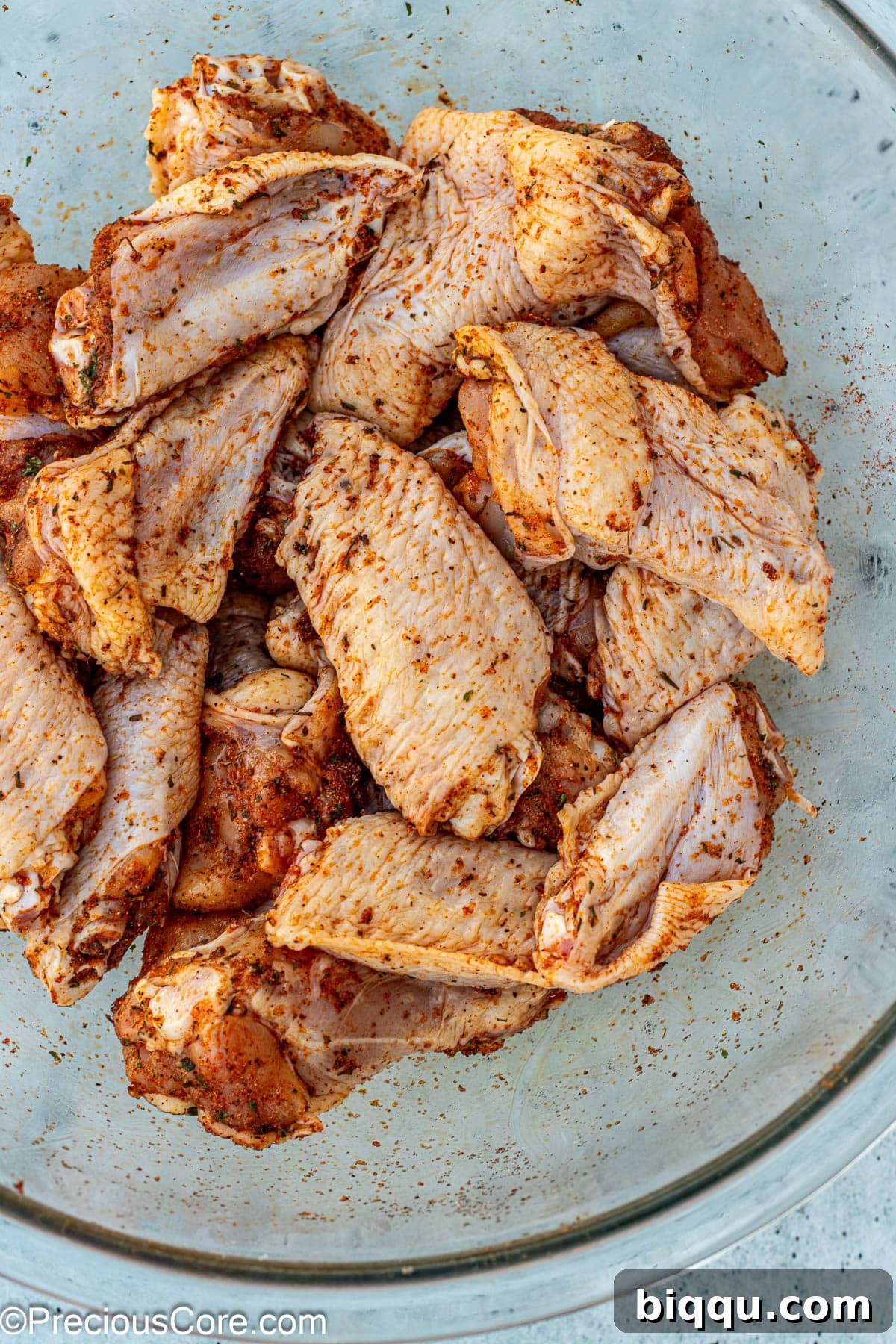 Chicken wings in a large mixing bowl, thoroughly coated with a rich, dark dry rub seasoning.