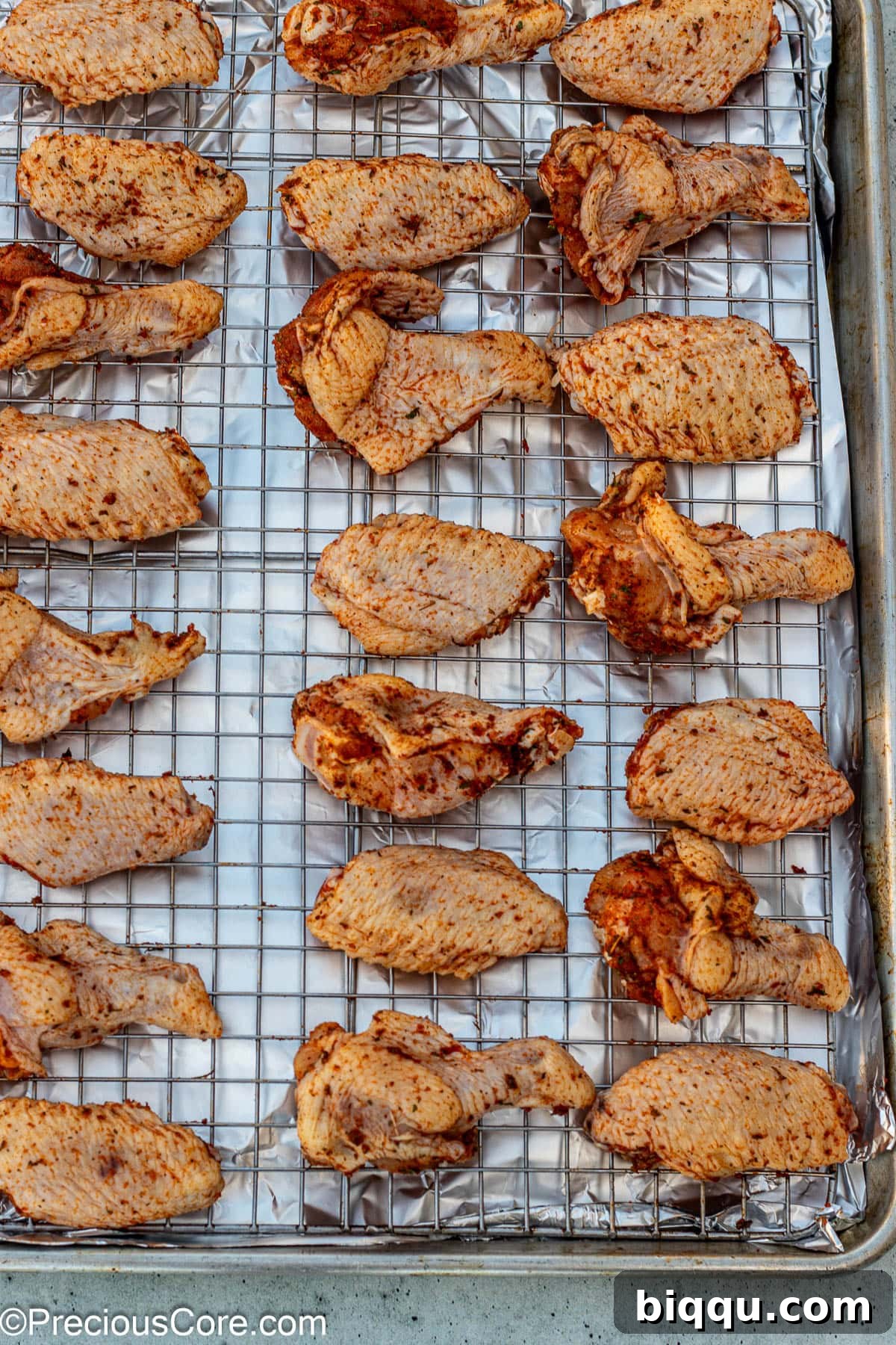 Raw, seasoned chicken wings arranged in a single layer on an oven-safe wire rack, placed over an aluminum foil-lined baking sheet.