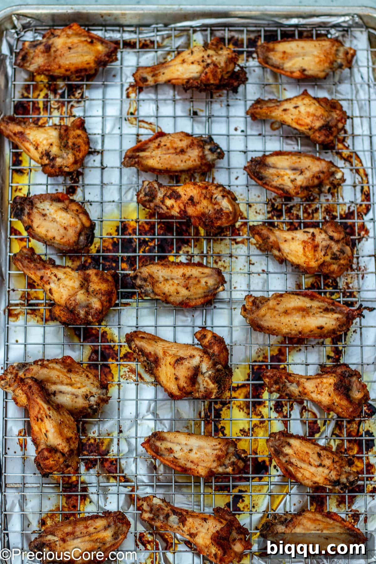 A batch of perfectly baked, golden-brown dry rub chicken wings resting on an oven-safe wire rack after being removed from the oven.