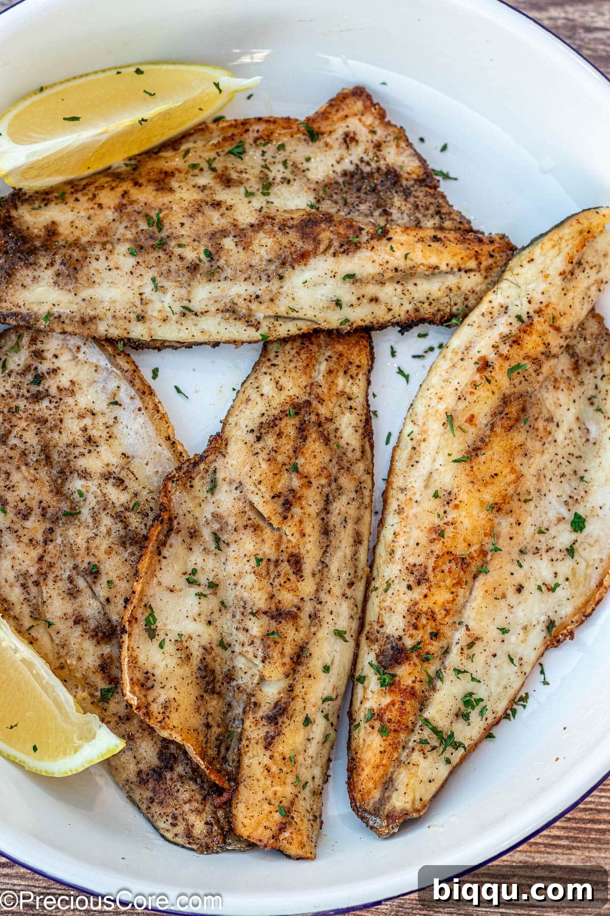 Pan Seared Sea Bass fillets on a white plate, garnished with fresh herbs.