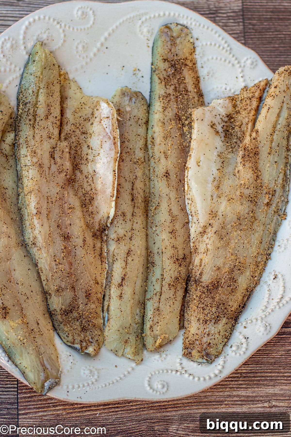 Seasoned sea bass fillets arranged on a large plate, ready for cooking.