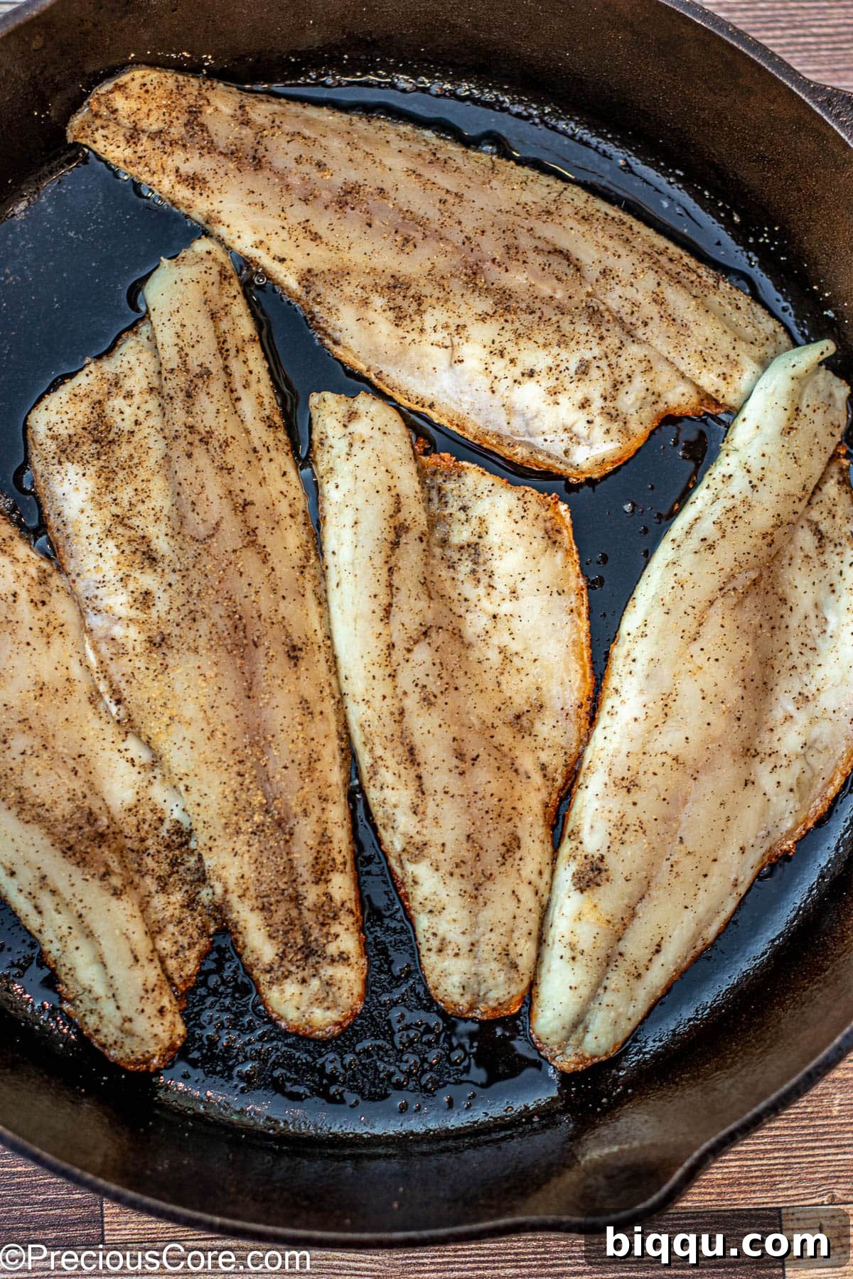 Multiple sea bass fillets cooking in a 12-inch cast iron skillet, skin side down.