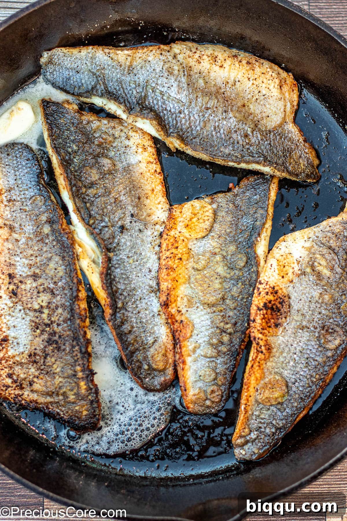 Butter melting and bubbling in a cast iron skillet around cooking fish fillets.