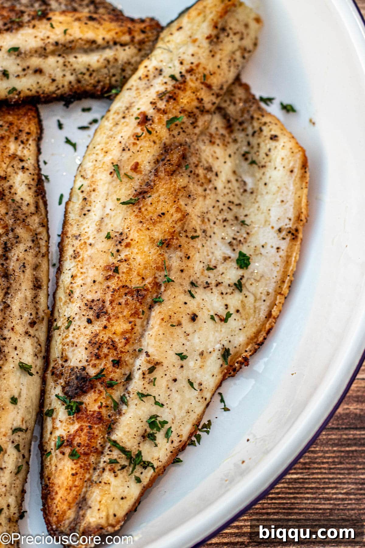 Plated Pan Seared Sea Bass garnished with fresh parsley and lemon wedges.