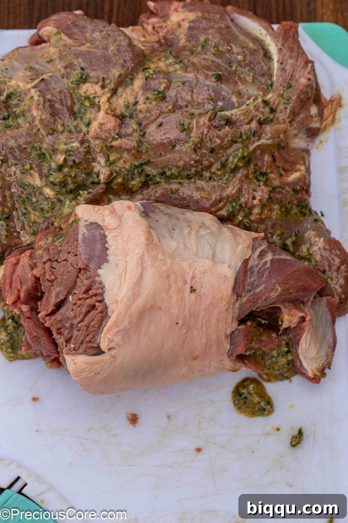 Rolling the butterflied boneless lamb leg tightly into a log shape.