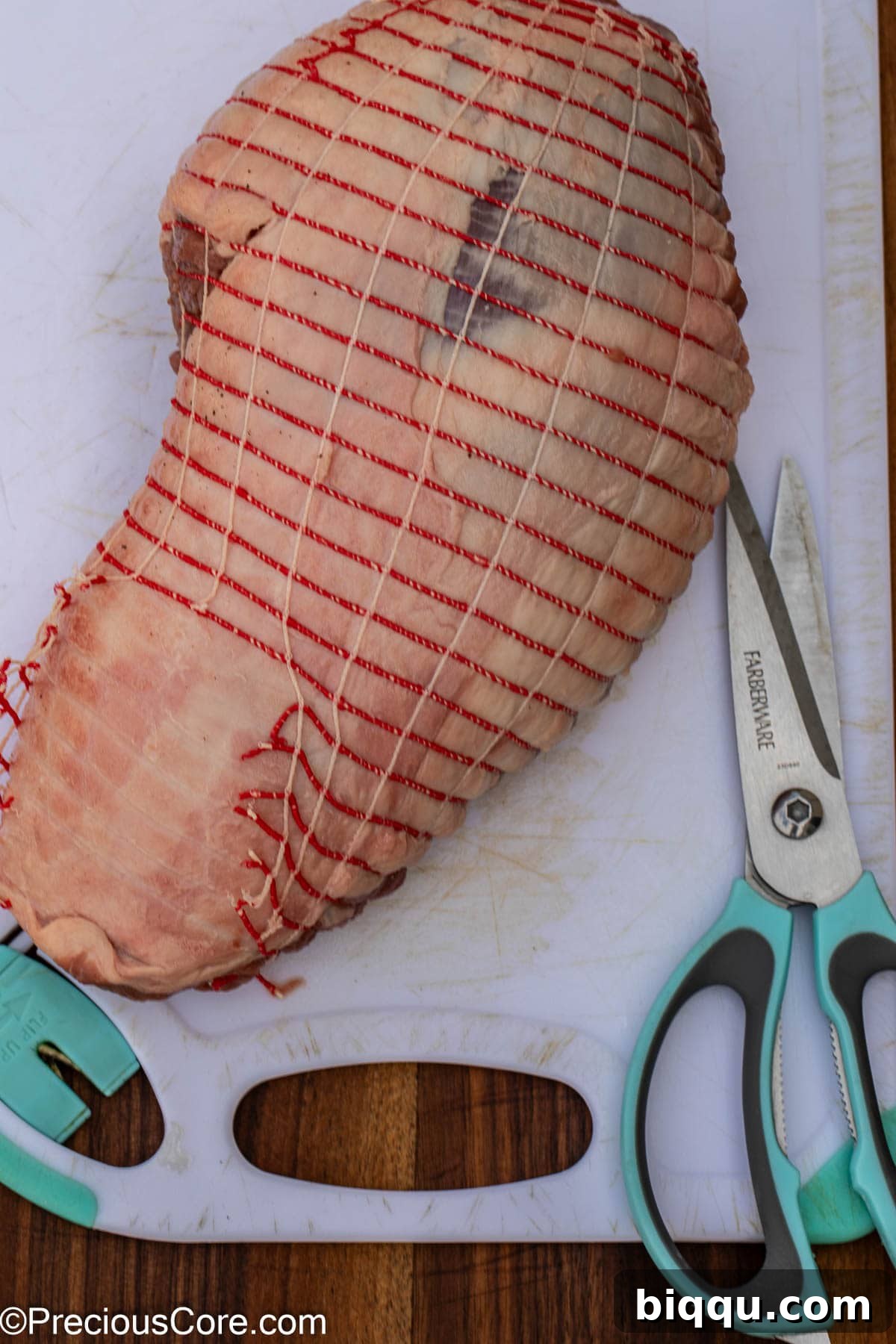 Carefully cutting off the covering or netting from the boneless lamb roast.