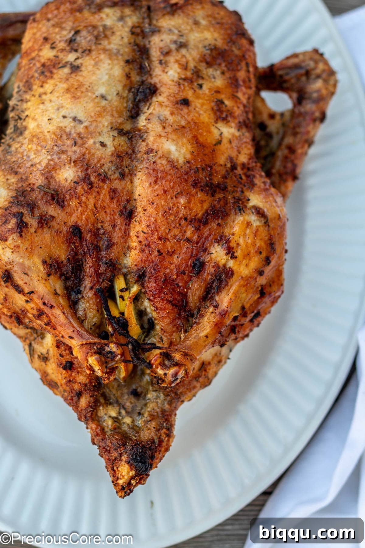 Herb roasted duck on a white serving tray, garnished with fresh herbs.