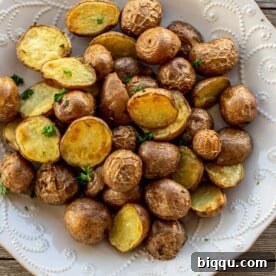 A large plate of golden brown roasted baby potatoes, seasoned with rosemary and thyme.