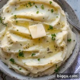 Square image of creamy rosemary garlic mashed potatoes, garnished with fresh herbs.