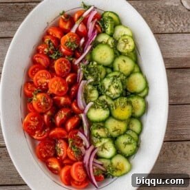 Refreshing tomato, cucumber, and onion salad with a zesty dressing on a platter.