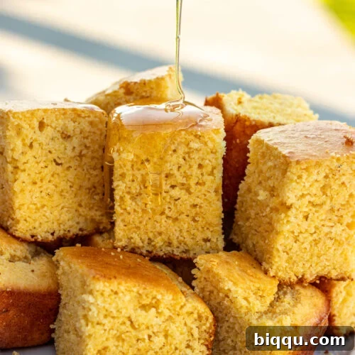 Square slices of cornbread without buttermilk with honey drizzling on top, a comforting side.