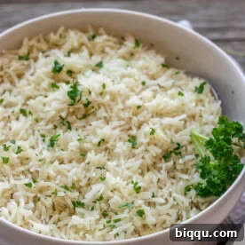 A bowl of garlic herb rice topped with minced fresh parsley, a savory pairing for chicken.