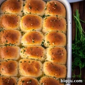A full baking dish of dinner rolls brushed with garlic butter, perfect for soaking up juices.