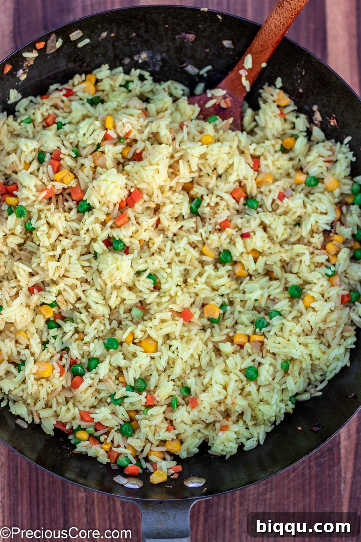 Rice being stir-fried with vegetables in a wok, beginning to absorb flavors.