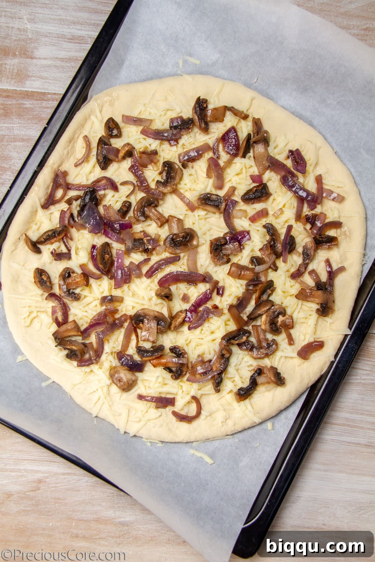 Uncooked pizza topped with mushrooms, cheese, and caramelized onions.