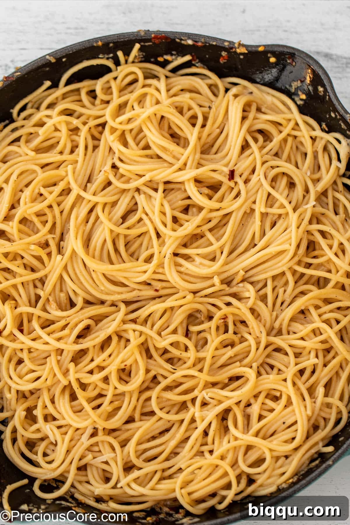 Close-up of spaghetti perfectly tossed and coated in a shiny garlic butter sauce within a skillet.