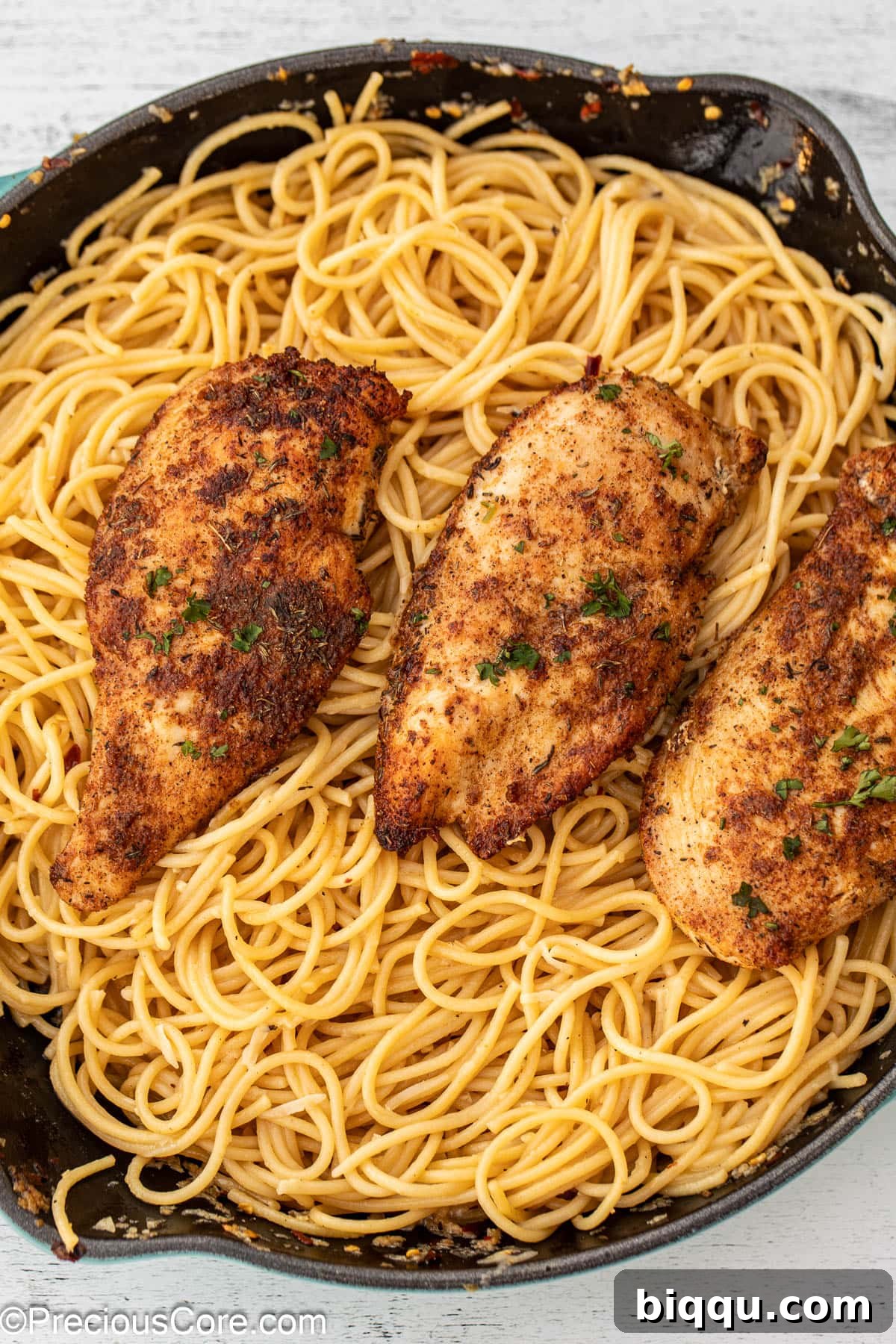 A rustic skillet filled with golden garlic butter spaghetti, generously topped with sliced, pan-seared chicken.