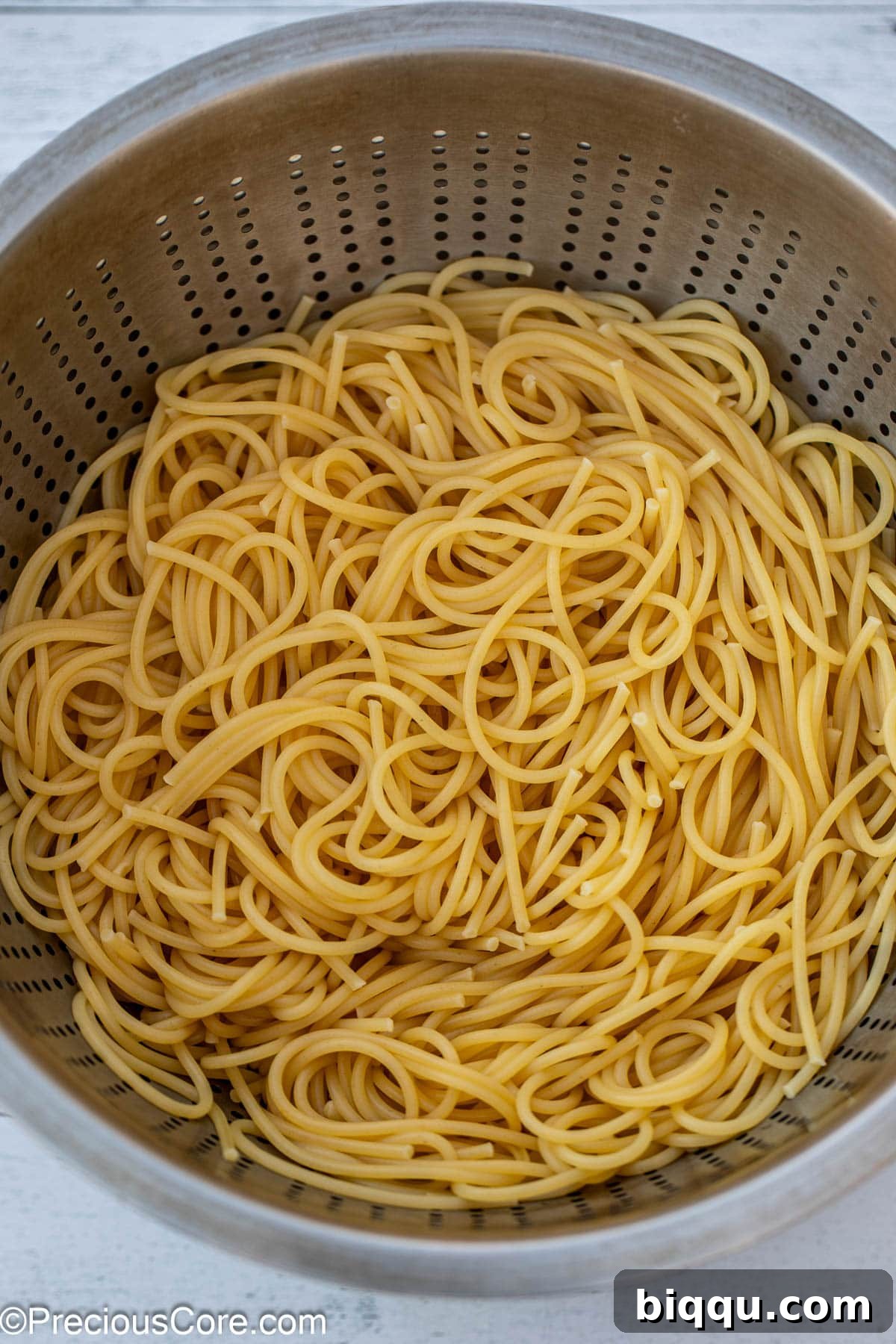 Freshly cooked and strained spaghetti noodles resting in a metal colander, steam gently rising.