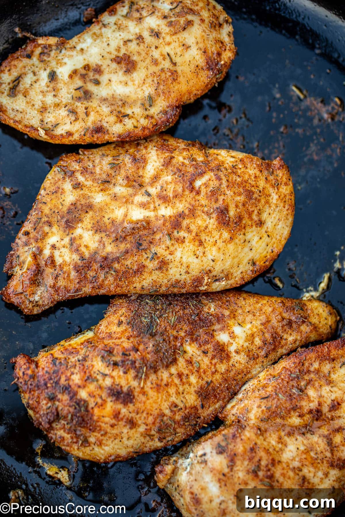 Two pieces of golden-brown pan-seared chicken breasts cooking in a hot skillet with olive oil.