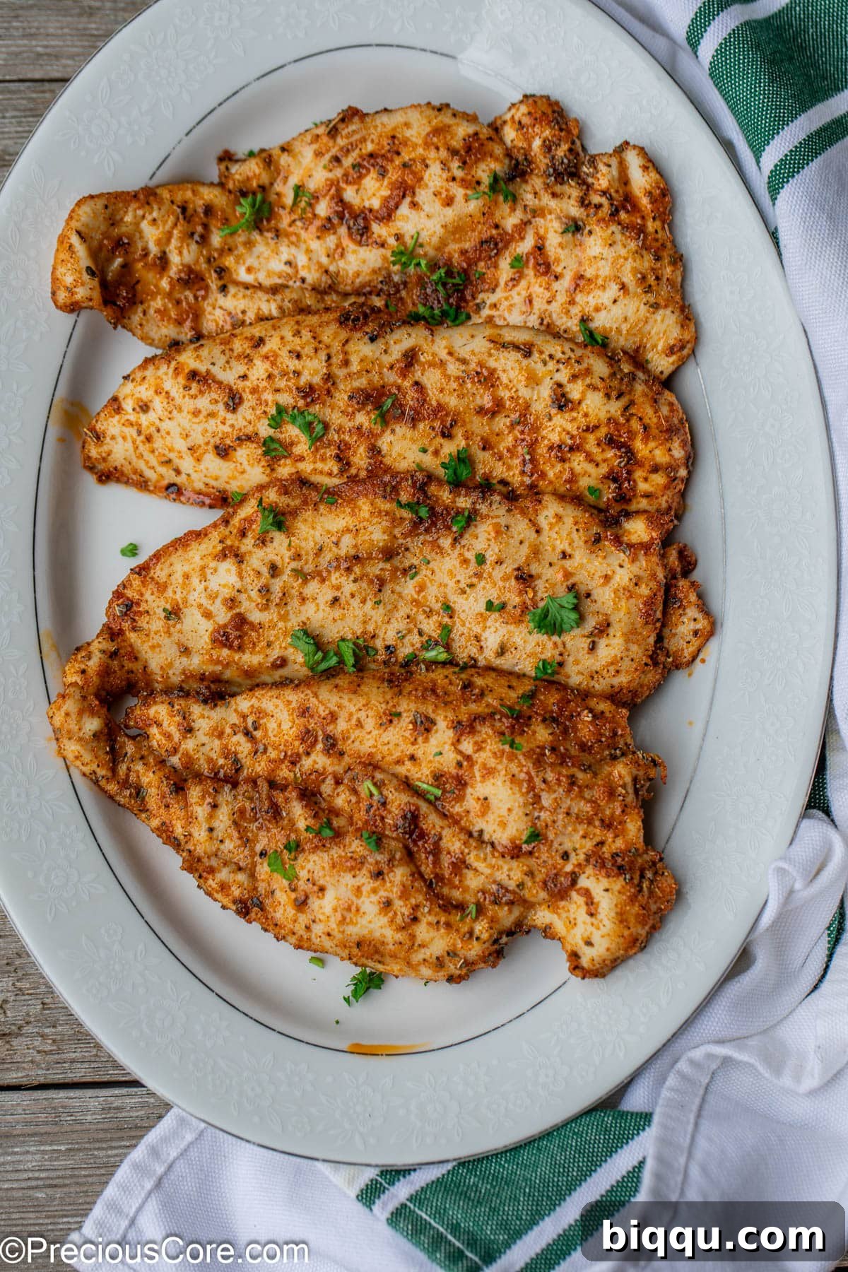 Cooked thin chicken breasts arranged beautifully on a pristine white serving plate, garnished with fresh herbs, highlighting their golden-brown finish.