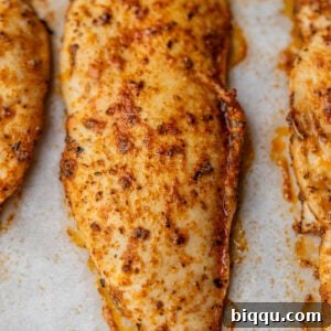Close-up of perfectly golden-brown, juicy baked chicken breasts, garnished with fresh herbs, ready to be served.