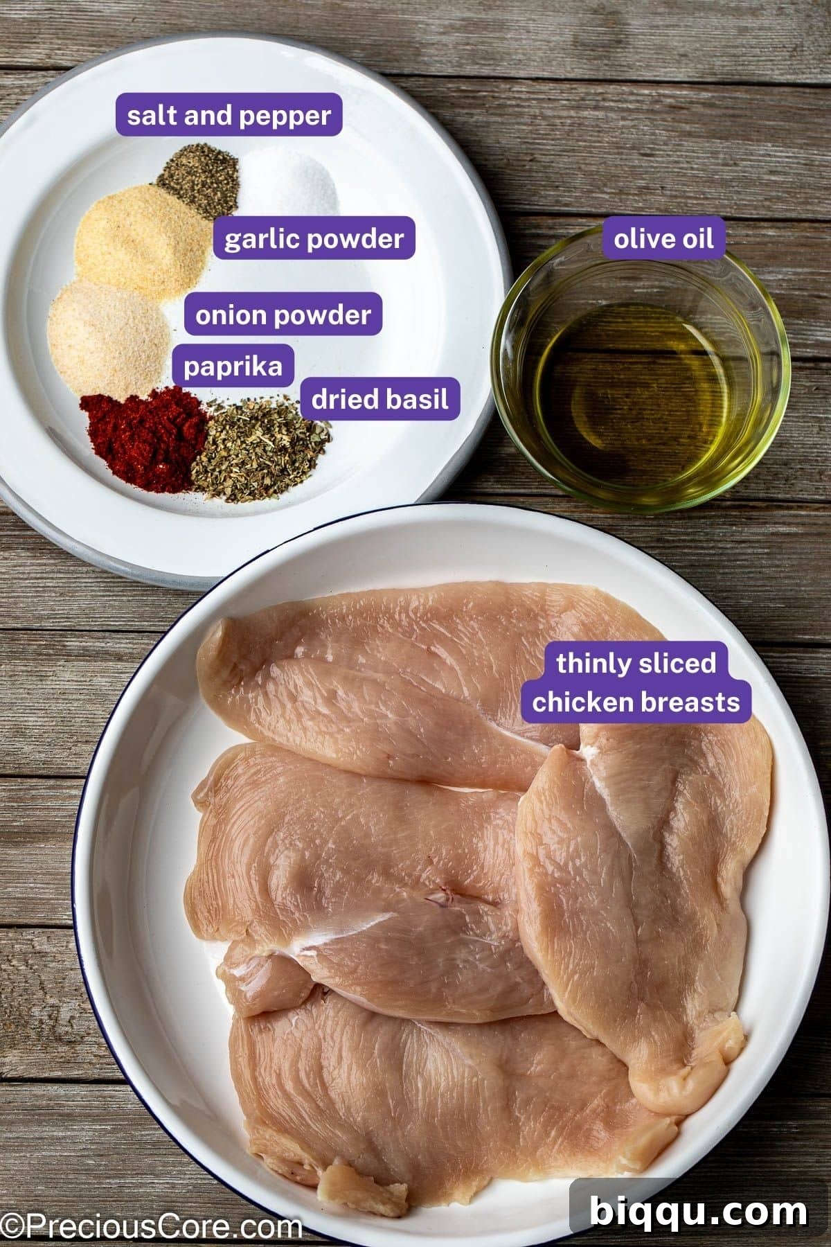A beautifully arranged spread of fresh ingredients on a wooden board, featuring thin chicken breasts, olive oil, and a selection of aromatic spices, all labeled.