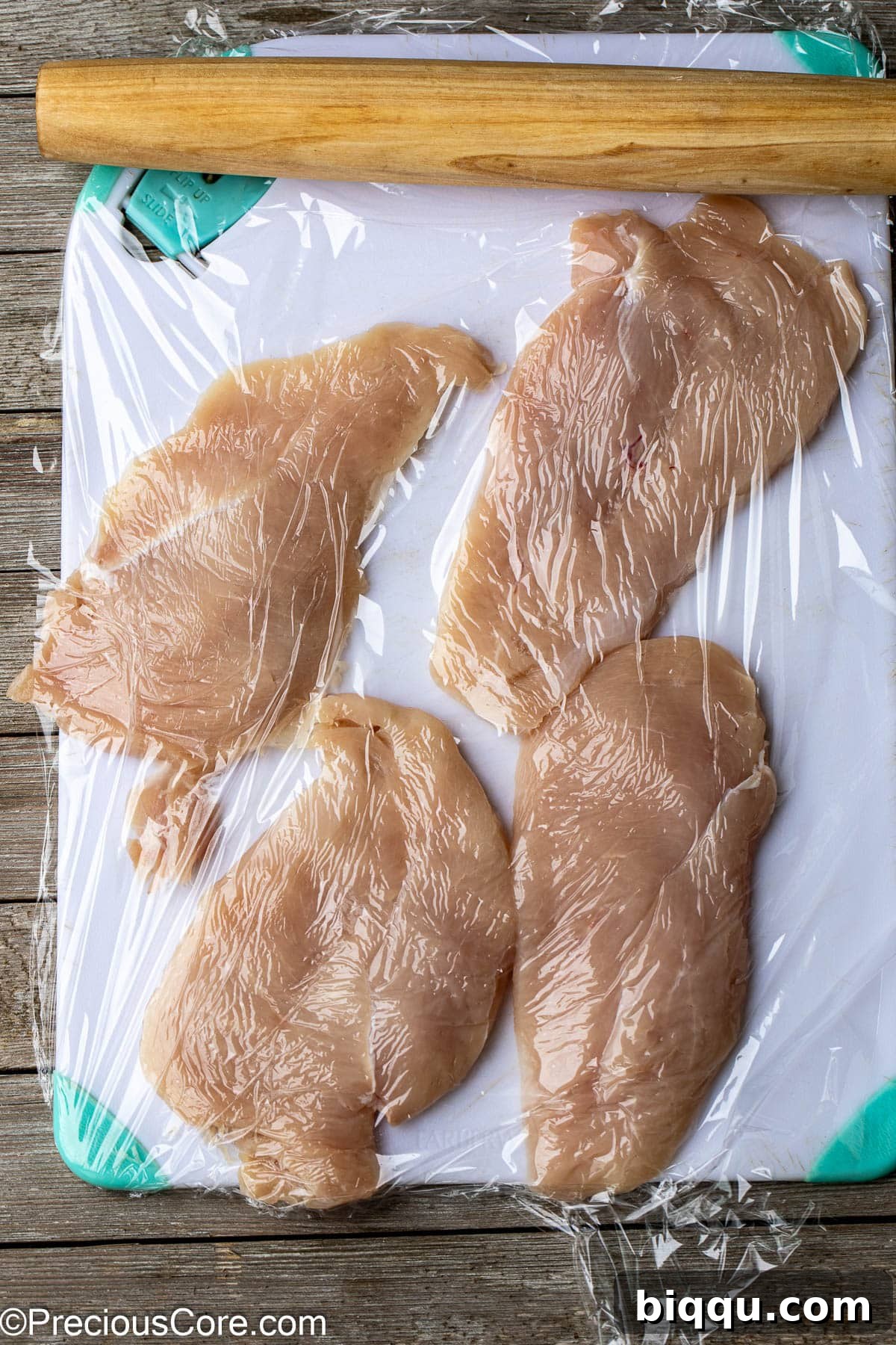 Chicken breasts being expertly flattened with a rolling pin on a chopping board, demonstrating a crucial step for even cooking.