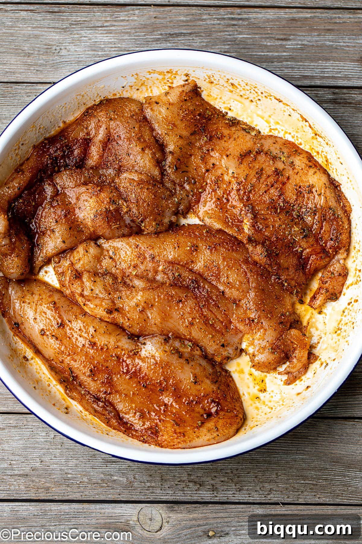 Seasoned thin chicken breasts nestled in a white bowl, thoroughly coated evenly with a vibrant and aromatic spice blend.
