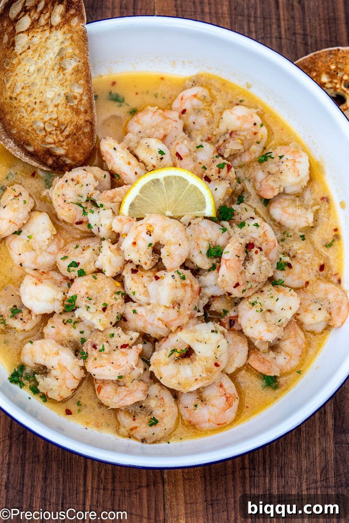 Crusty bread in a bowl of shrimp in white wine sauce, ready to be enjoyed.