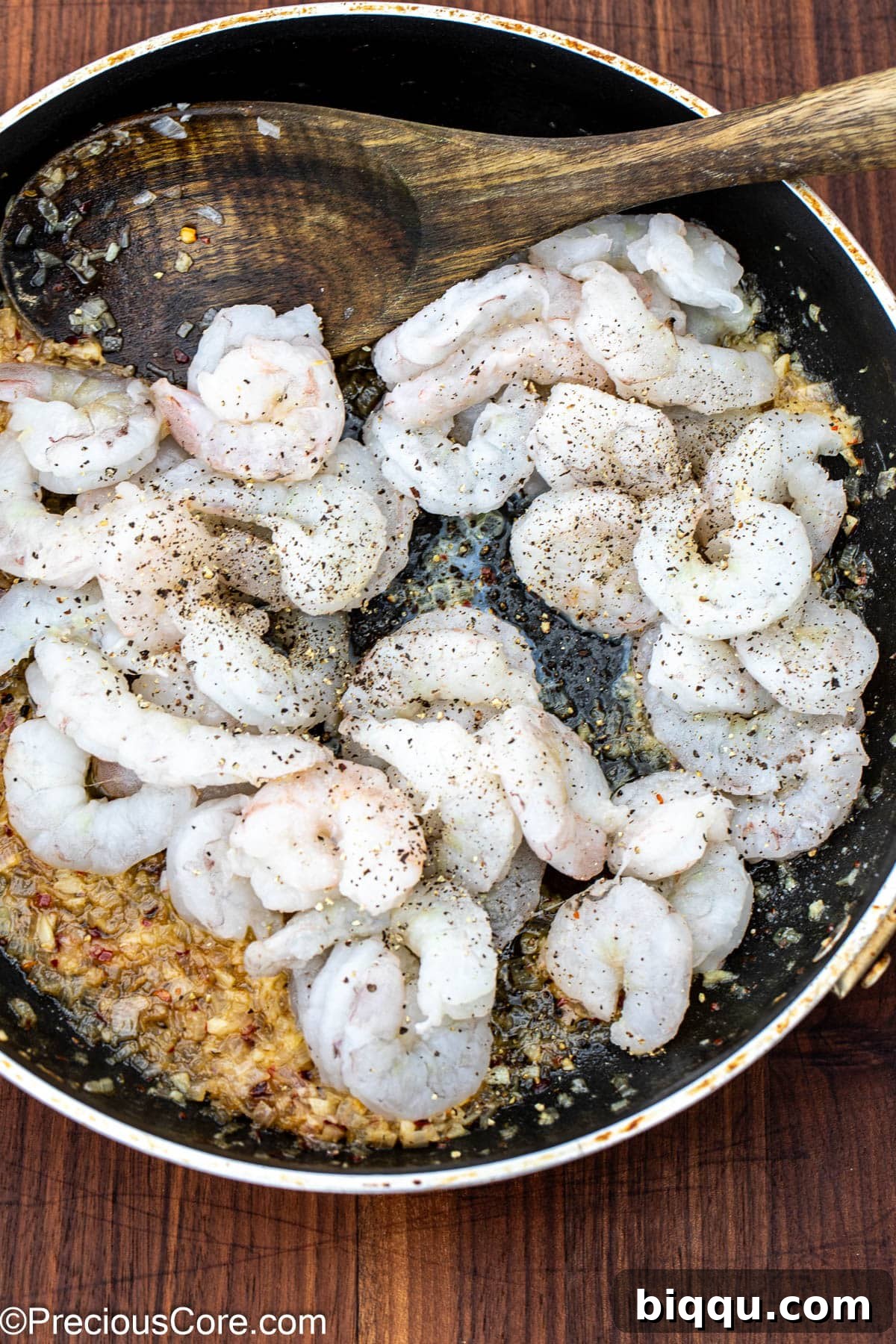 Raw shrimp added to the skillet, sprinkled with salt and black pepper, ready to be cooked.