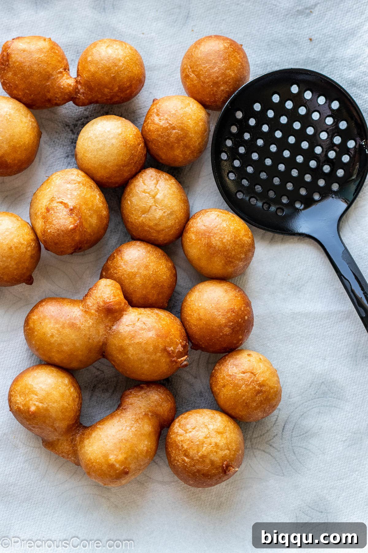 A generous pile of golden-brown, fried Puff Puff resting on paper towels in a white bowl, ready to drain excess oil.