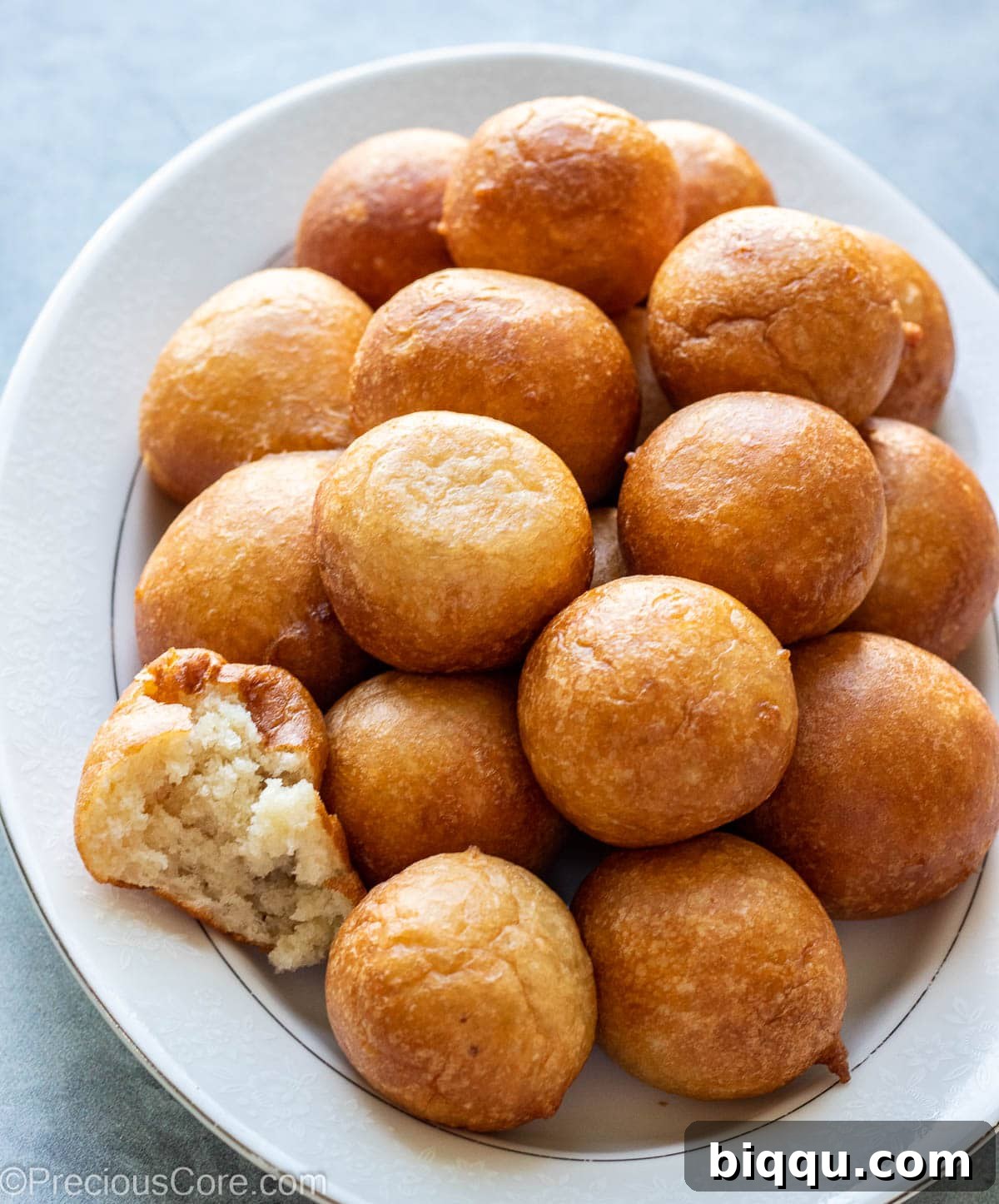 A white tray filled with golden Puff Puff, with one piece cut in half to reveal its airy, soft interior.