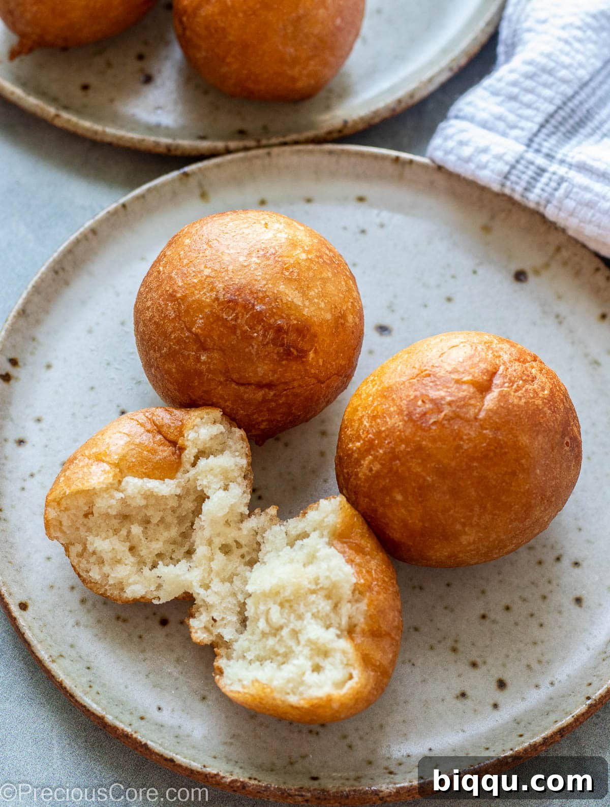 Three perfectly round Puff Puff balls on a plate, one opened to showcase its light and fluffy texture.