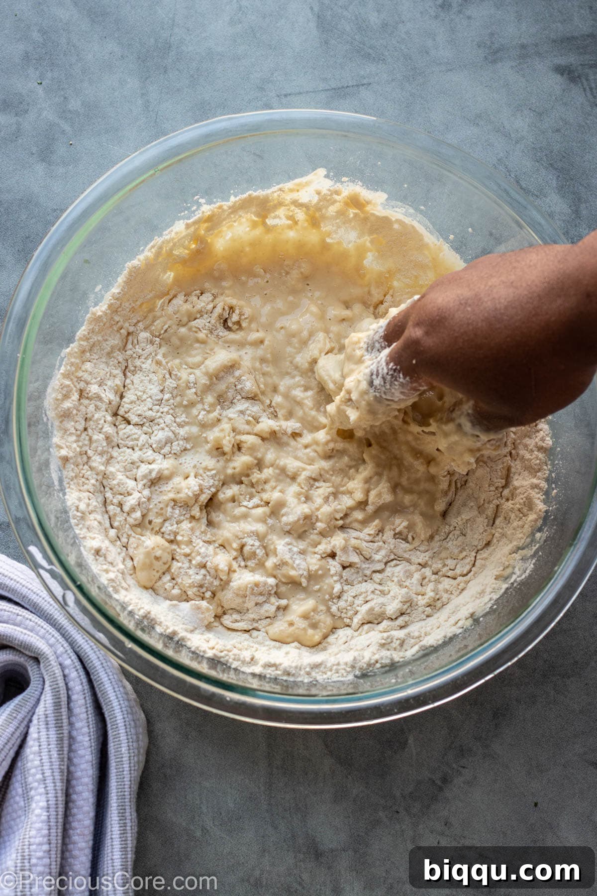 A hand mixing the Puff Puff batter in a large white bowl with a wooden spoon, ensuring all ingredients are well combined.