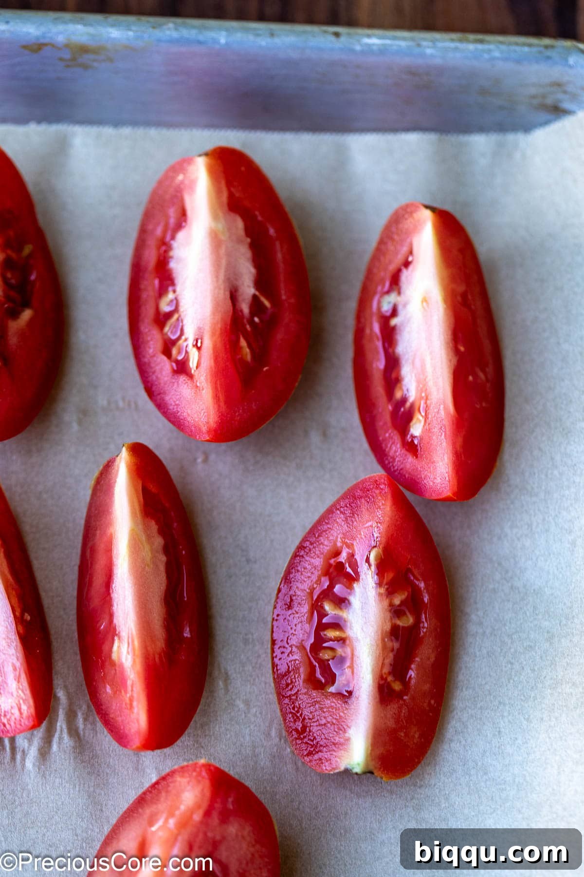 Roma tomatoes cut into quarters and arranged on parchment paper on a baking sheet.