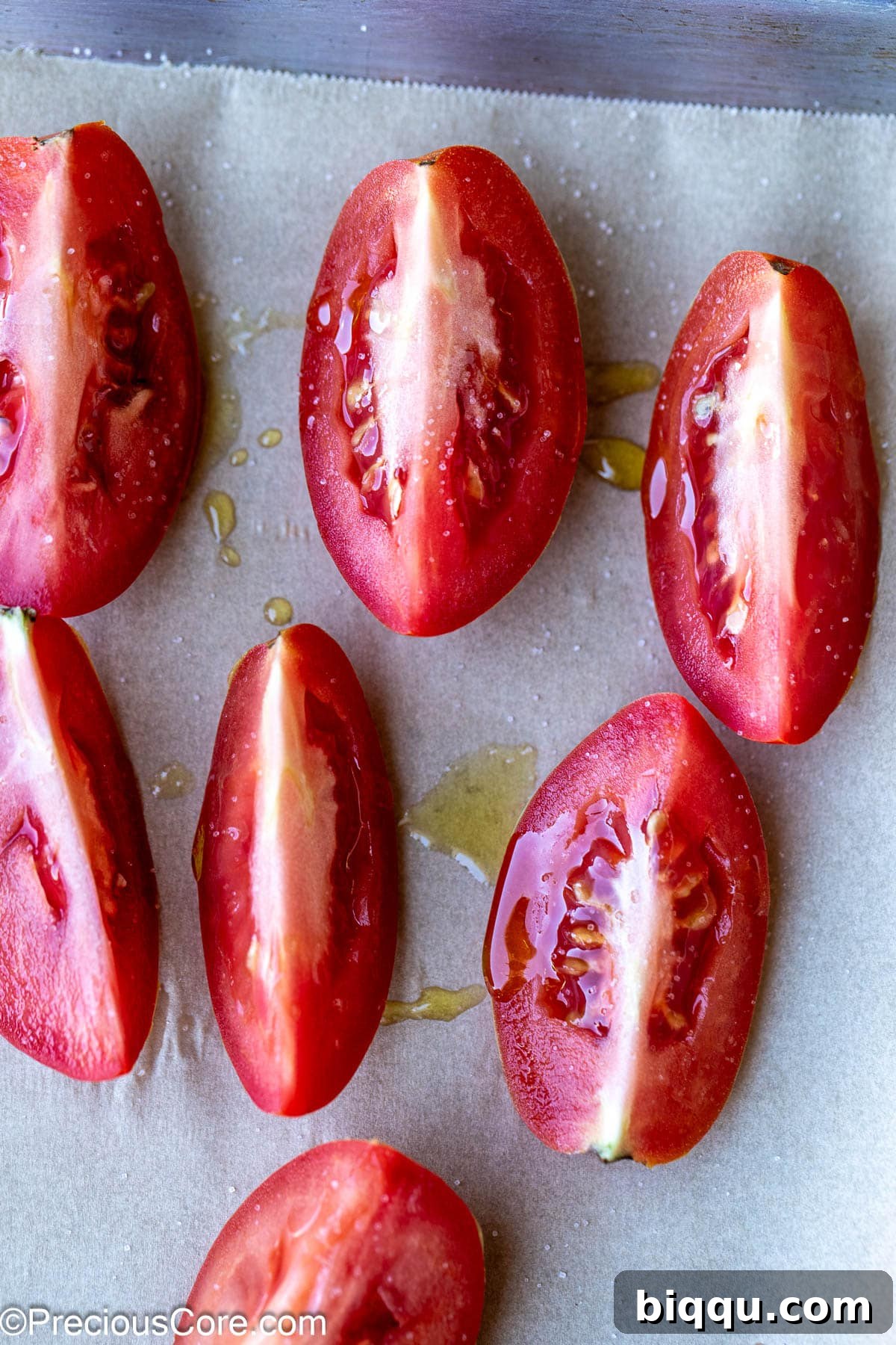 Tomato quarters drizzled with olive oil and sprinkled with salt on a baking sheet.