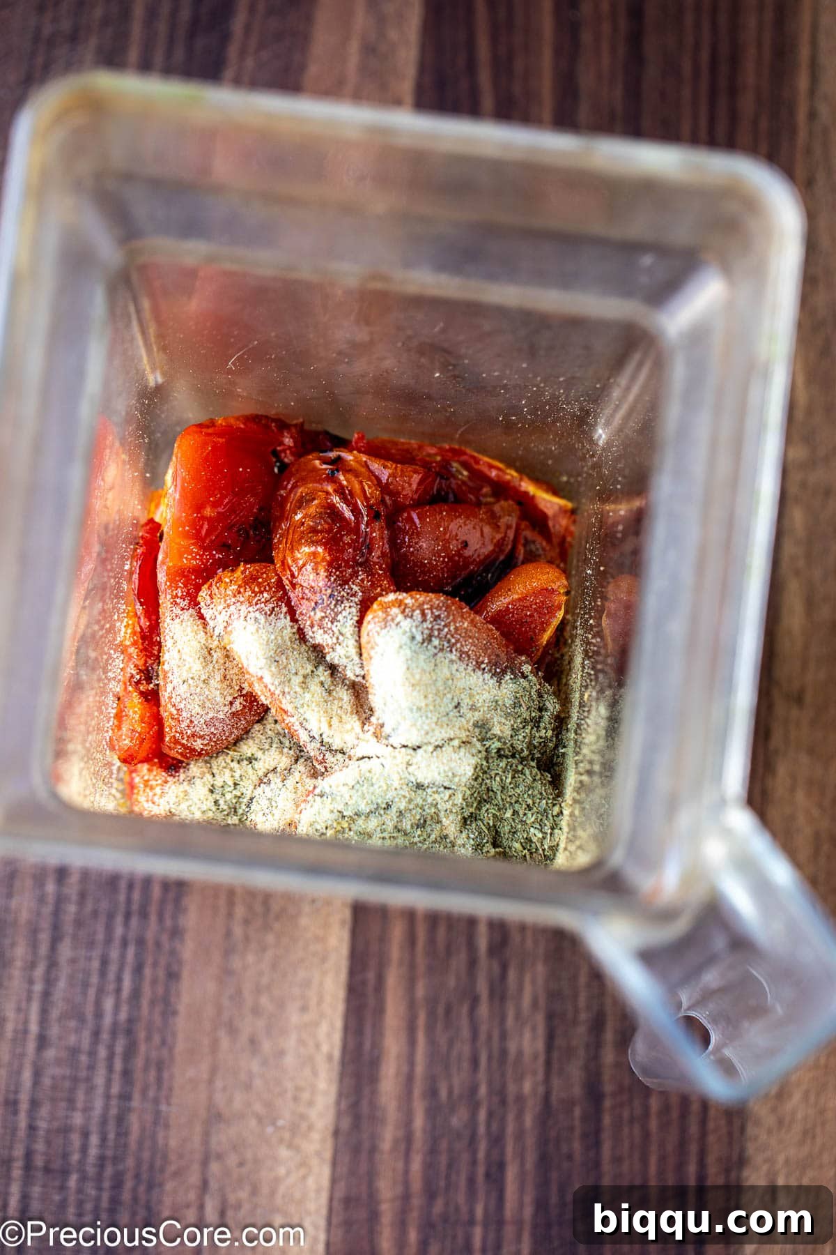 Roasted tomatoes and spices being added to a blender.