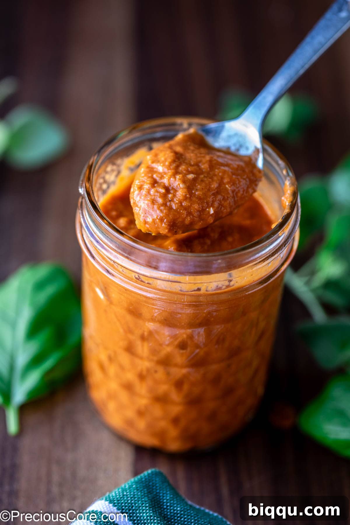 A spoon scooping a generous amount of rich, red roasted tomato pizza sauce from a bowl.