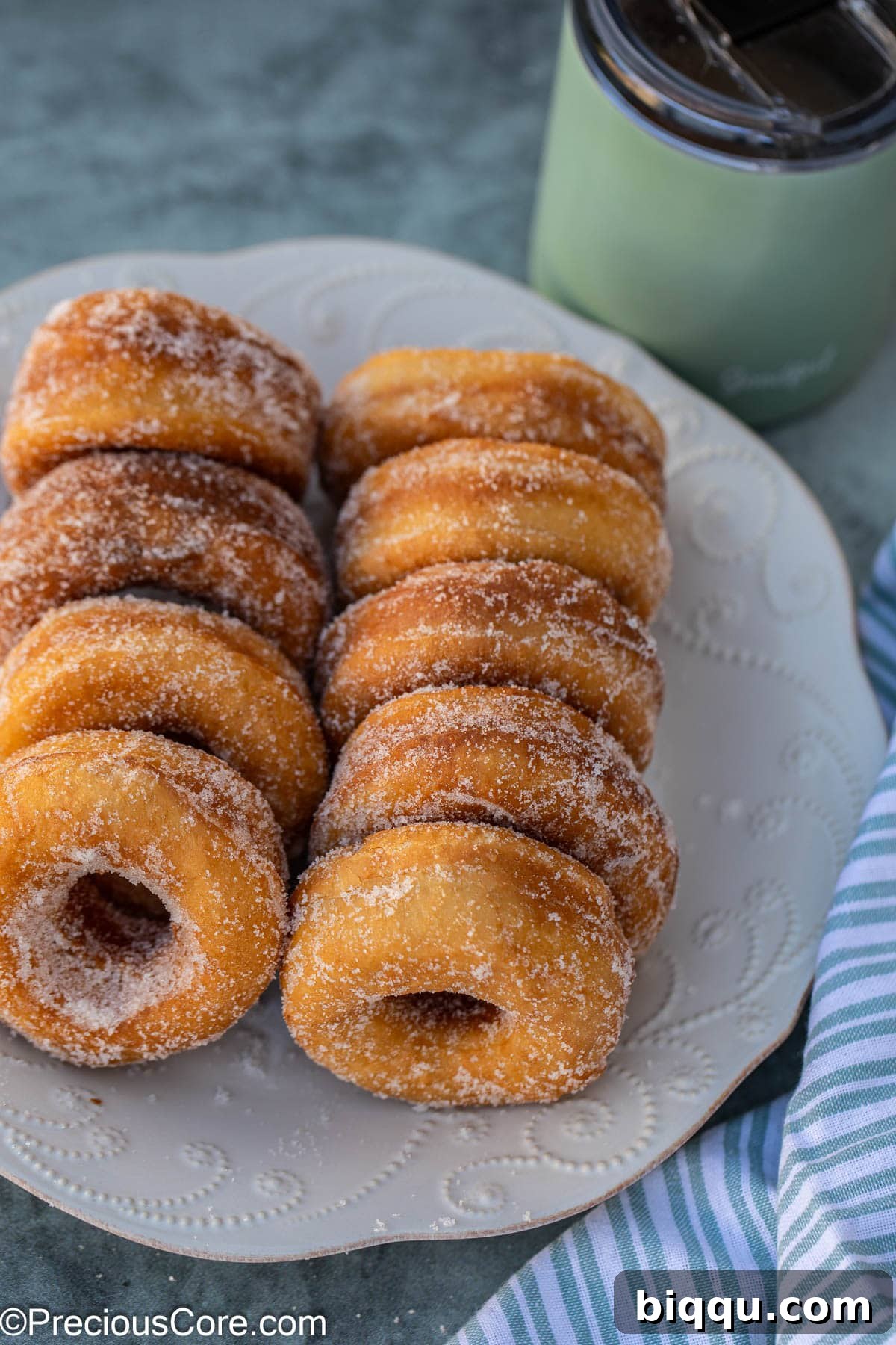 Nine sugar coated donuts on a white plate.