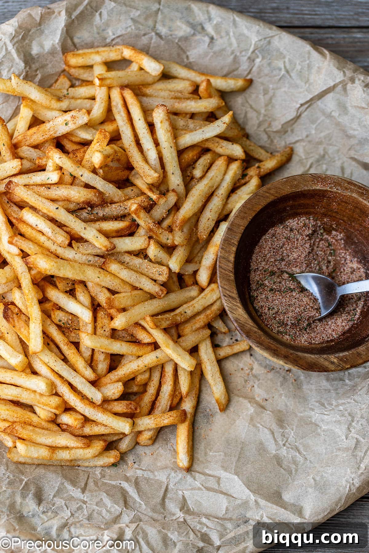 Crispy French fries on brown parchment paper with a generous sprinkle of golden seasoning.