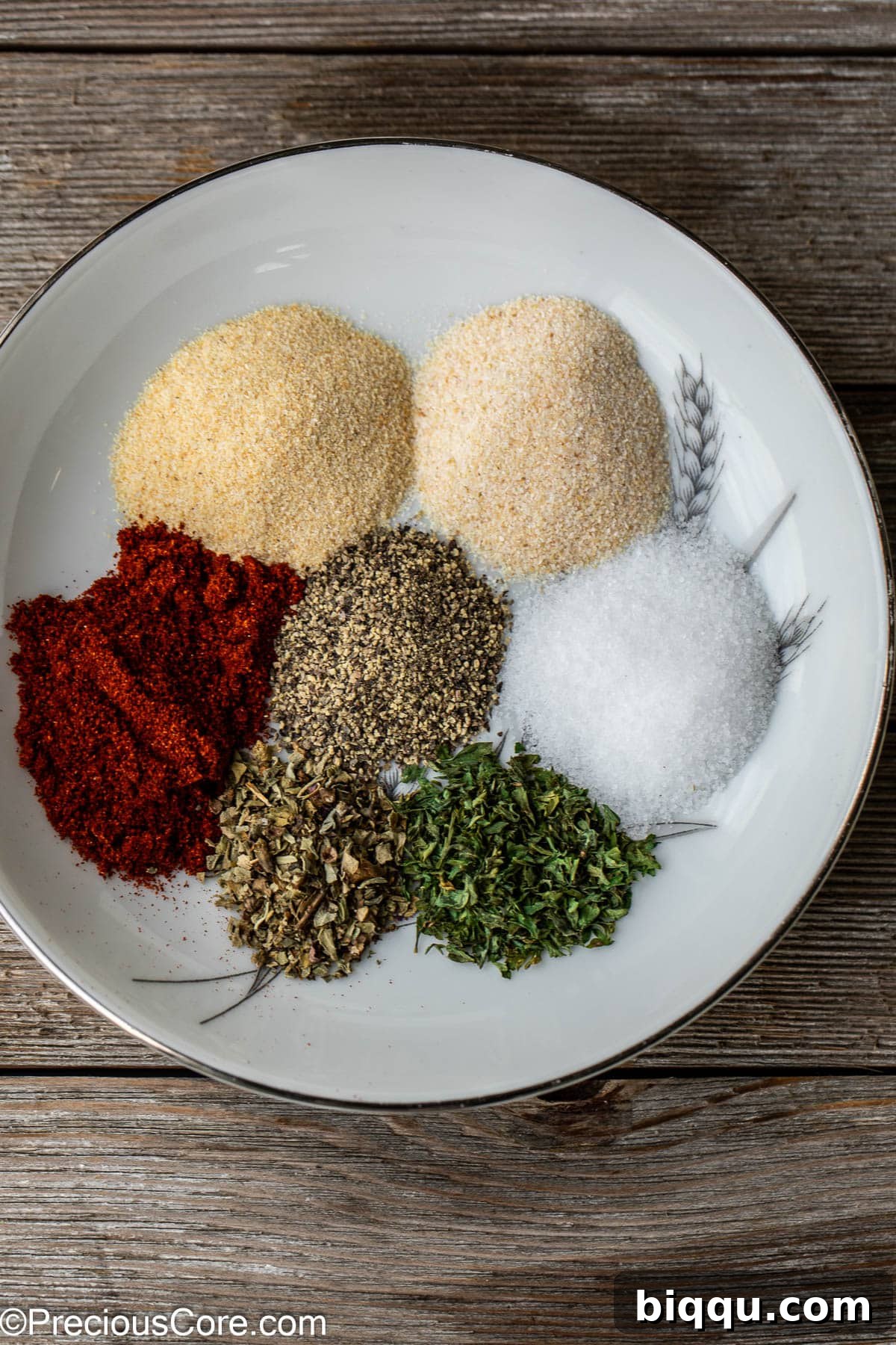 Various individual spices laid out on a white plate, ready to be blended for French fry seasoning.