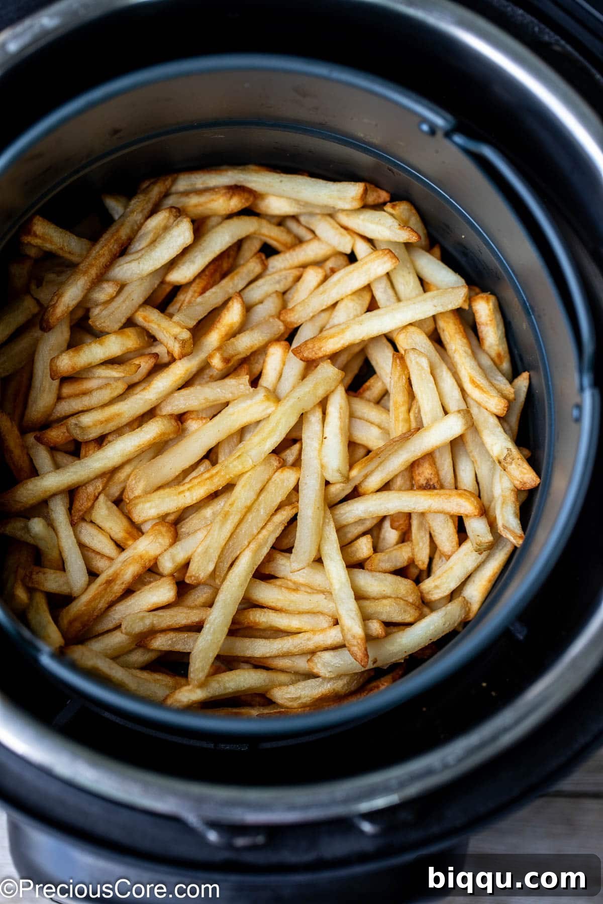 Crispy air-fried French fries in a round air fryer basket, ready to be served.