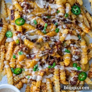 Loaded French Fries on a sheet pan, perfectly golden with melted cheese and crispy bacon, garnished with green onions.