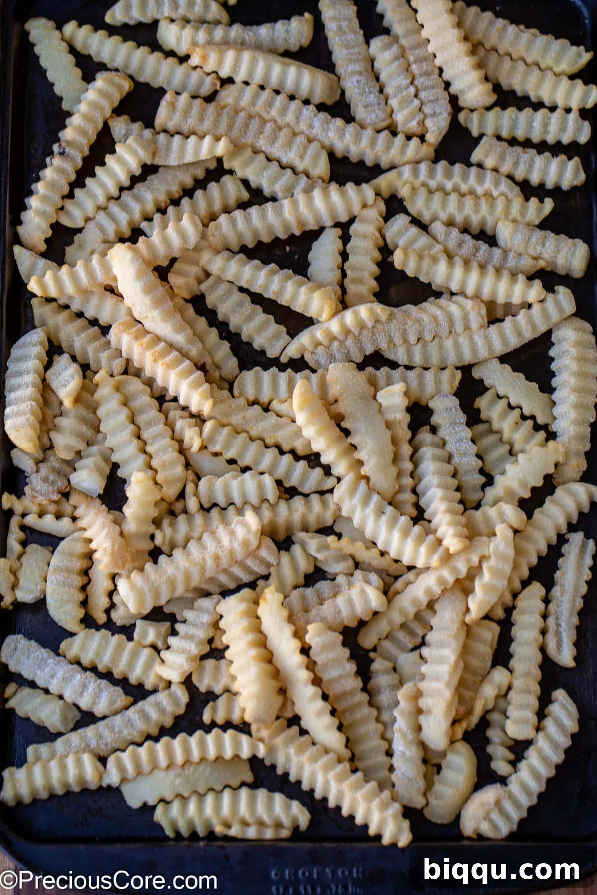 Frozen French fries spread evenly on a baking sheet, ready for cooking.