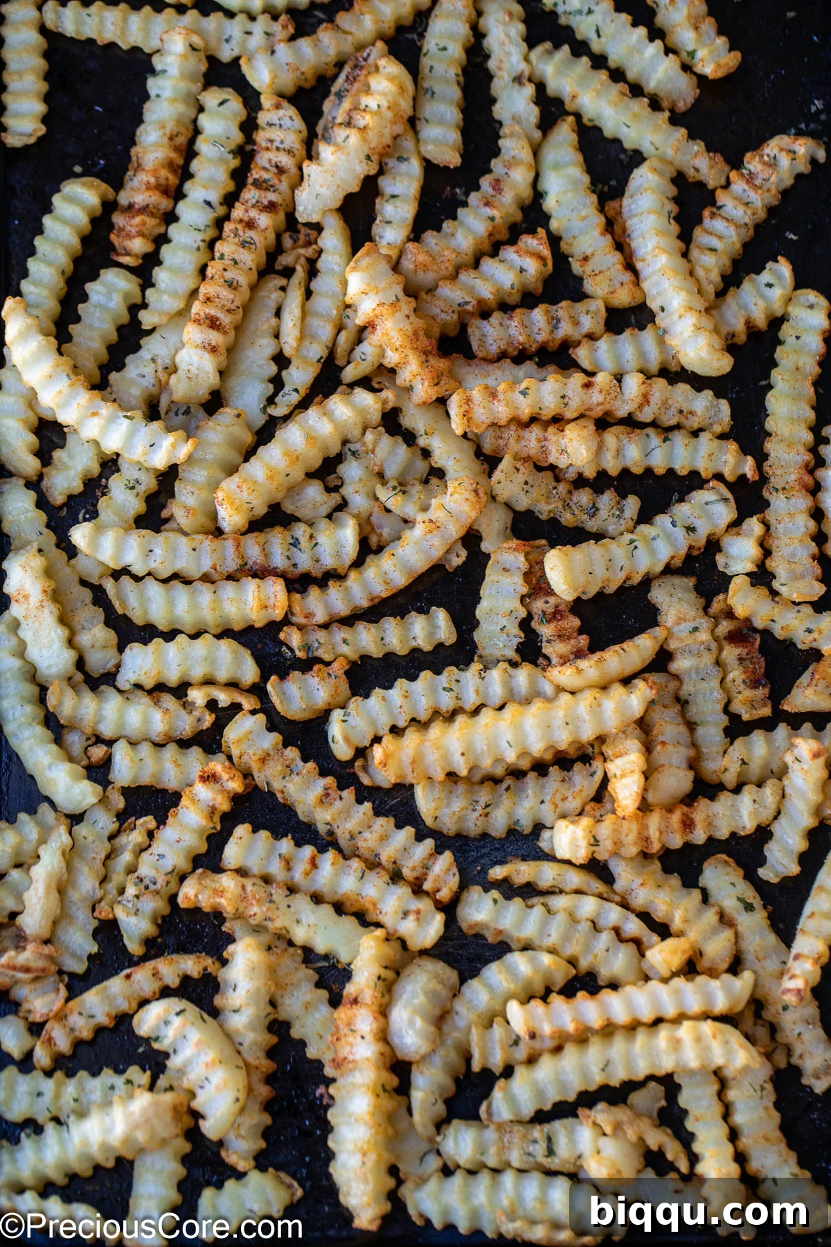 Seasoned crinkle-cut fries freshly cooked and spread on a sheet pan, showing their crispy texture and golden color.